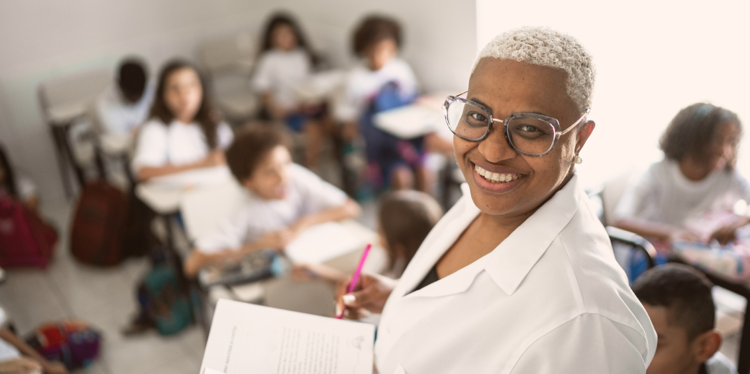 Teacher with a classroom full of students, smiling at camera.