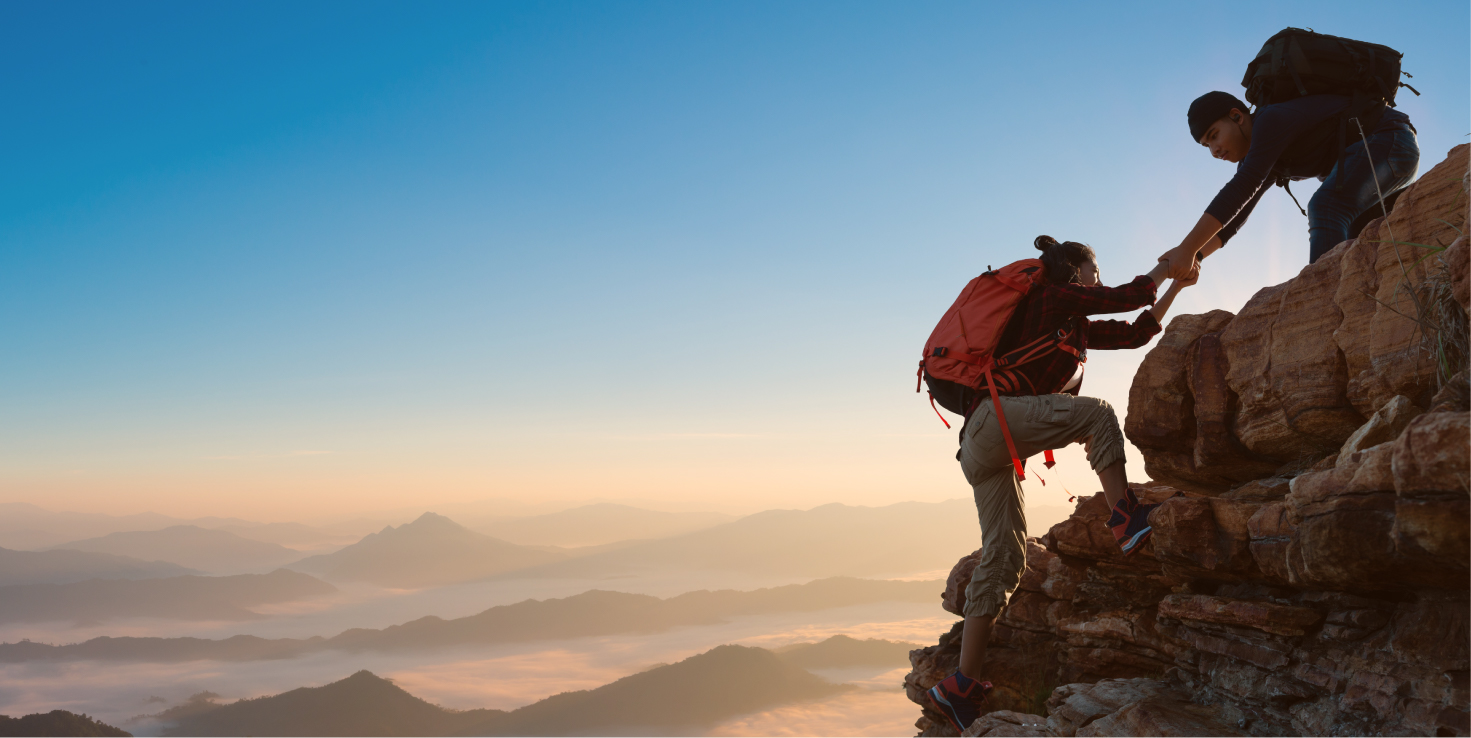 Couple helping each other hike up a mountain.