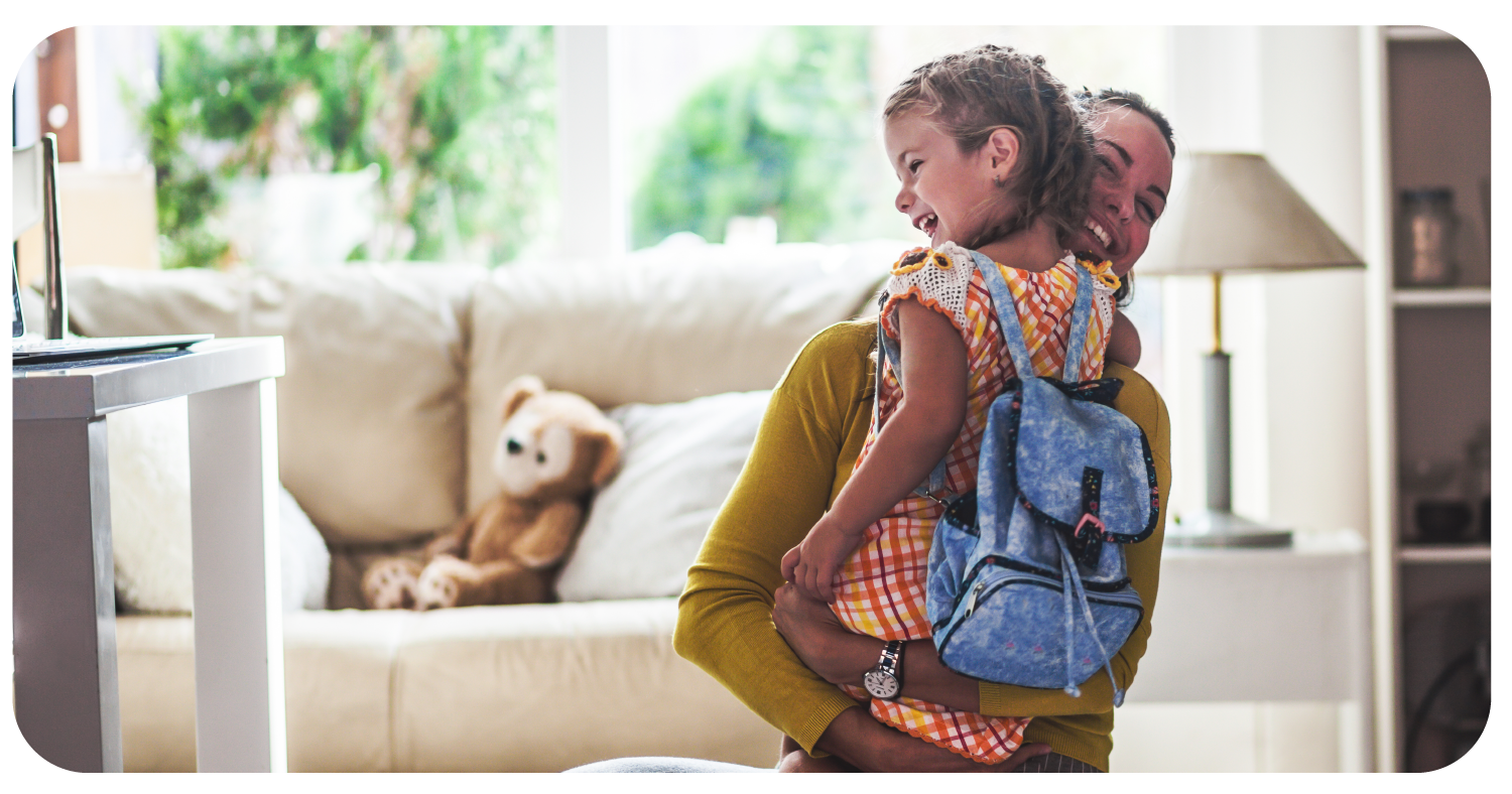 Mother embracing smiling young child before sending her off to her first day of school.