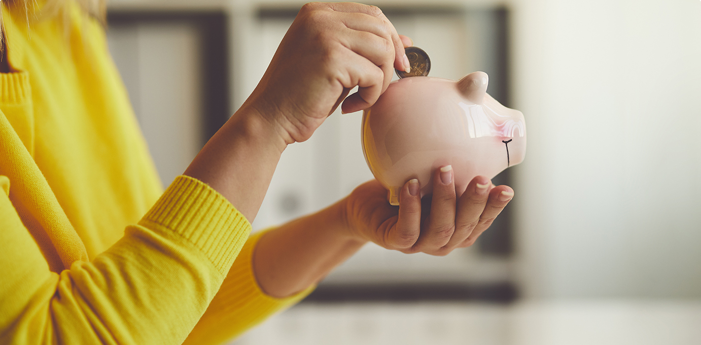 A woman in a yellow sweater adding coins to a piggy bank.