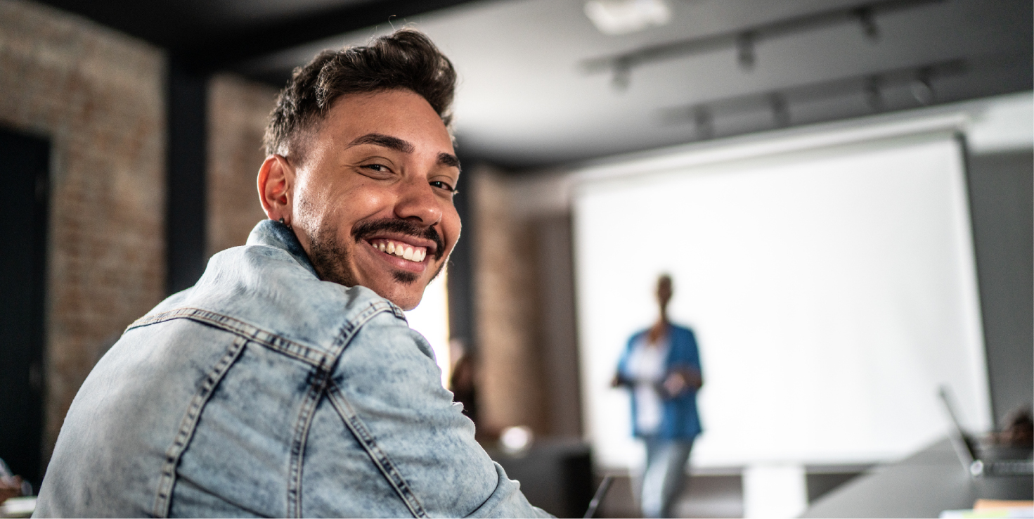 Man in a classroom, looking over his shoulder smiling at the camera.